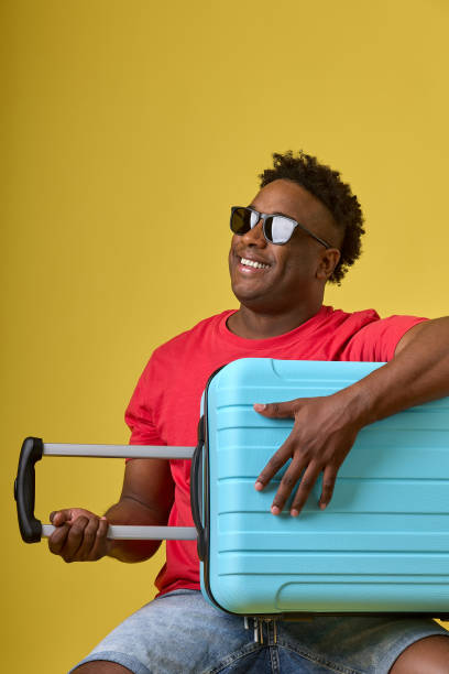 istock Dark-skinned man in sunglasses smiles while holding large suitcase in his hands 1709992404