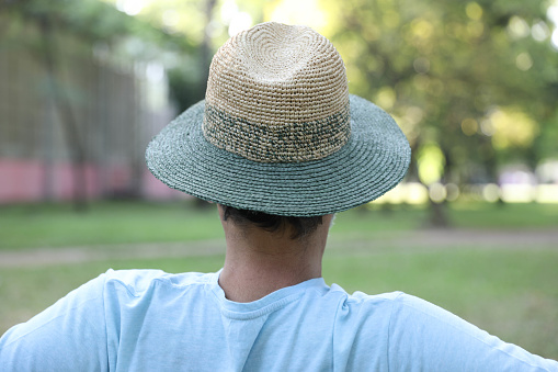 Rear view of a lone man with a hat sitting alone on a park bench.