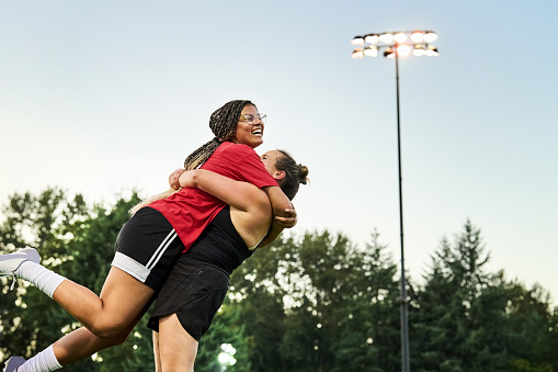 Shot of two female soccer players embracing and celebrating a goal while playing on outdoor sports field
