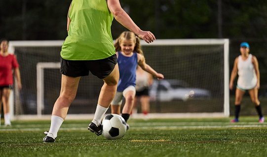 Low section of female player playing soccer with little girl on soccer field