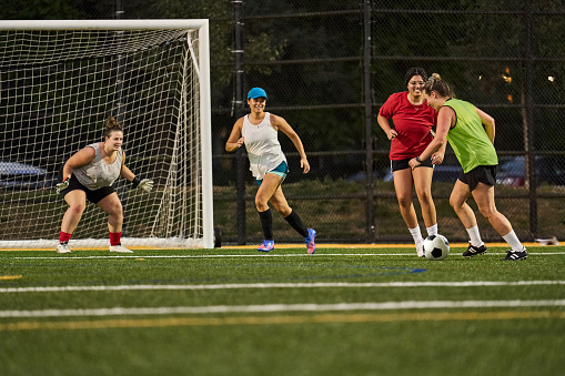Team of young women playing a scrimmage on a sports field during a soccer practice in evening