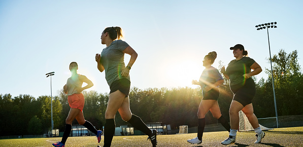 Group of young women in sports clothing running together outdoors during a team soccer practice