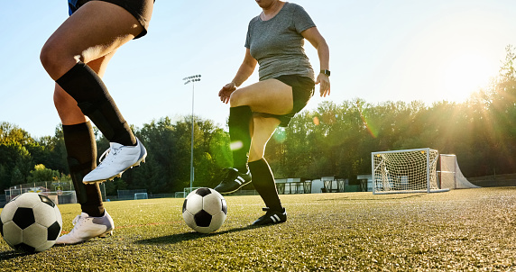 Cropped shot of women soccer players doing drills with balls during practice on a sports field on sunny day