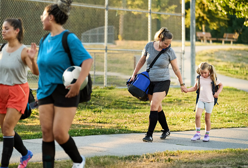 Group of young women and a girl in sports clothing leaving the field after soccer practice session