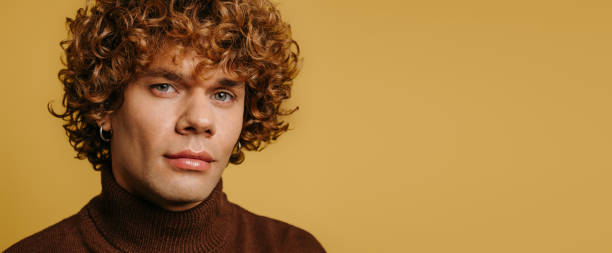 istock Handsome young curly man in sweater looking at camera against yellow background 1710075990