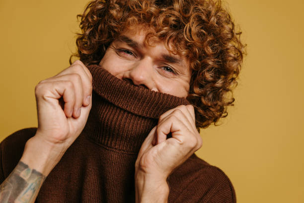 istock Handsome curly young man hiding half face behind a sweater neck against yellow background 1710076536