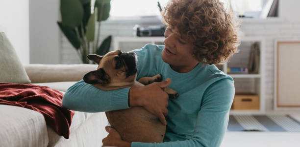 istock Handsome young curly man holding his cute dog and smiling while relaxing at home together 1710078400