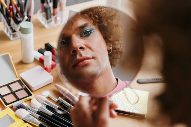 istock Confident young gay man looking at his reflection in the mirror while applying make-up 1710081181