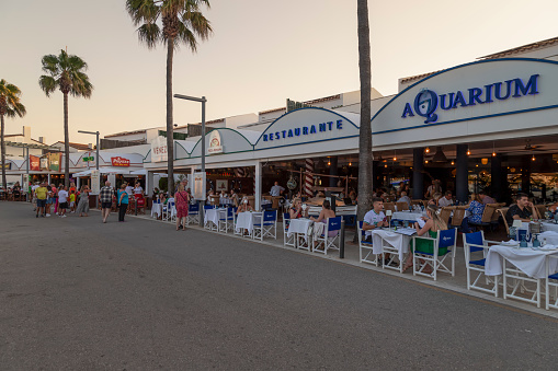 Cala en Bosc, Spain, June 22, 2023; Tourists strolling past the cozy restaurants on the harbor in the seaside resort of Cala en Bosc on the Spanish island of Menorca.