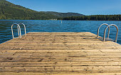Wooden pier with metal ladder into the sea, lake. Swimming dock pier with ladder on lake at sunny day on idyllic resort