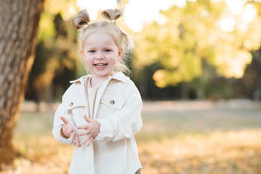Laughing blonde child girl 4-5 year old having fun over nature background outdoor. Autumn season. Childhood.