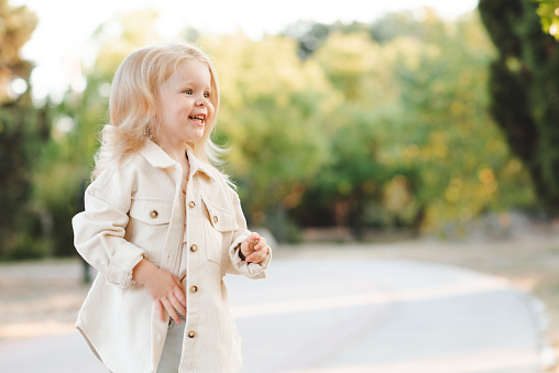 Laughing blonde child girl 4-5 year old wear jacket over nature background outdoor. Autumn season. Childhood.