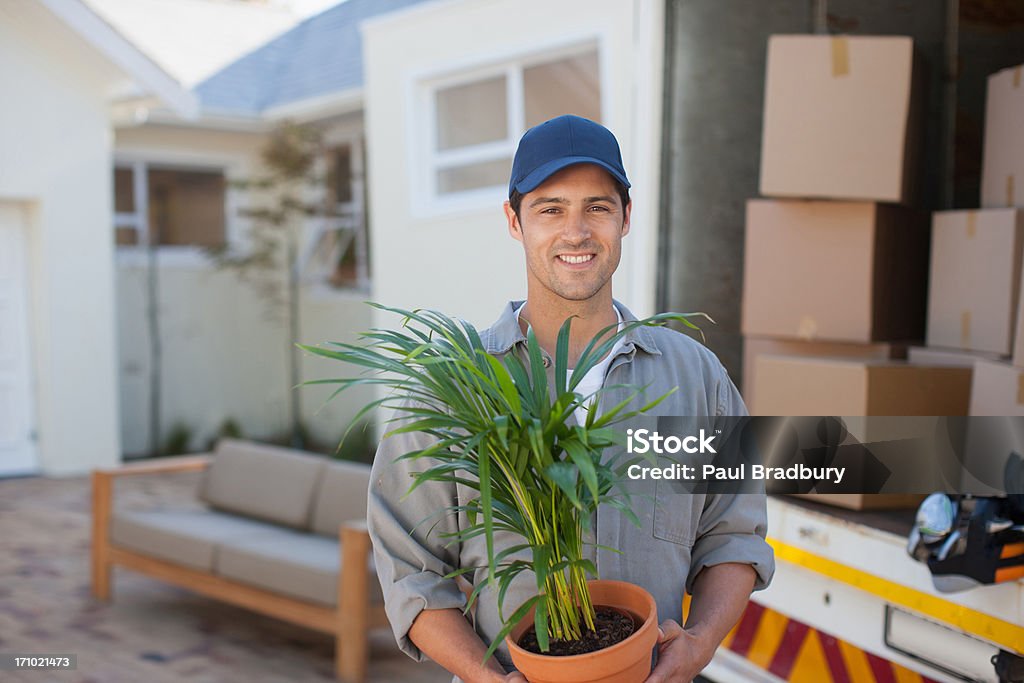 Uomo sorridente che trasportano Flowerpot Camion per autotrasporti - Foto stock royalty-free di Berretto da baseball