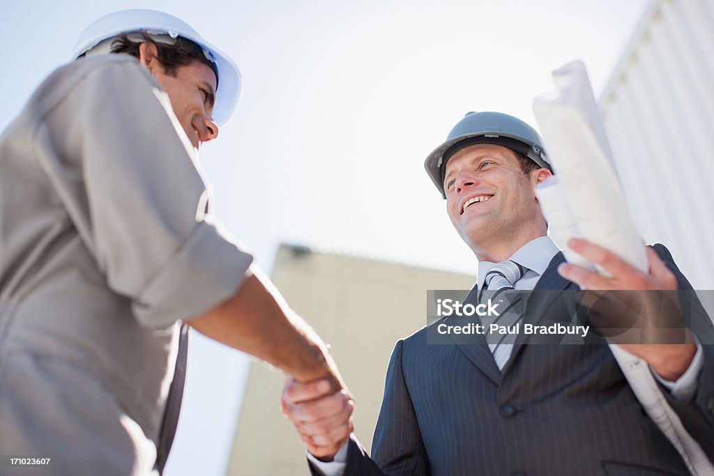 Businessman with blueprints shaking hands with worker  Construction Site Stock Photo