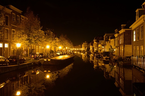A fleet of boats in a canal in front of a picturesque row of houses at night: Leiden