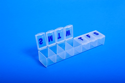 Clear plastic weekly pill organizer open through Wednesday set on blue background. High angle view