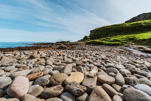 Low angle view of large pebbles in the pristine water Lake Michigan, with puffy clouds in the blue sky above the teal horizon.