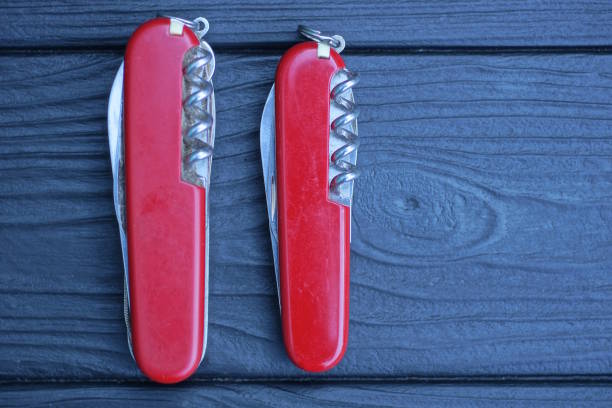 two closed folding knives with red handles lie on a black wooden table