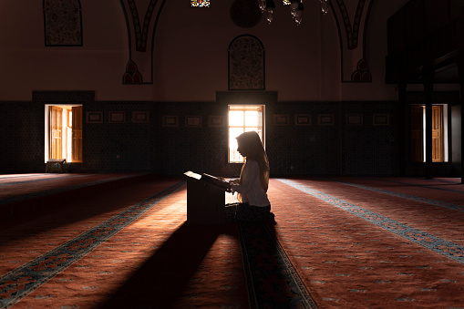 A girl reading the Koran in a mosque. Reading the Koran, the holy book of Islam. Girl praying in a mosque. Worship during Ramadan.   Miraj Kandil. Laylat al-Qadr. Regaip Kandil.