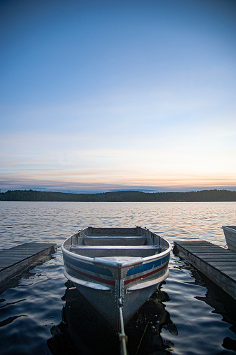 A metal rowboat sits tied to a lakeside dock at sunset