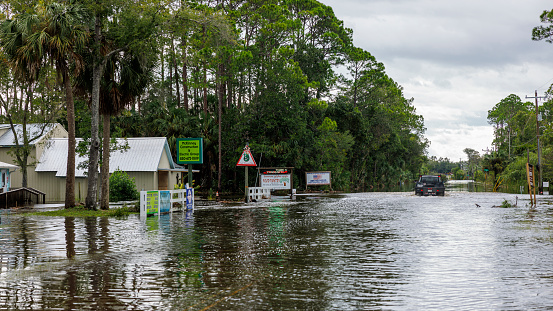 Steinhatchee, North Florida,  USA - August 30, 2023: flooded residential street and road in small community Steinhatchee, North Florida. Houses and trees underwater, pickup truck driving in the distance. Hurricane landfall and flood aftermath