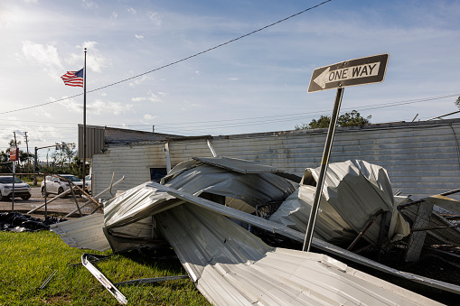 Demolished parts of shop and twisted roof after storm: destructed store building in Perry, North Florida. Road sign and American flag rise above debris
