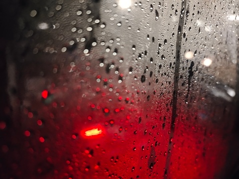 Raindrops cling to the windshield at night and red lights from motorcycle taillights
