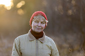 Smiling, mature woman in red hat, standing in the forest in early winter at sunset.