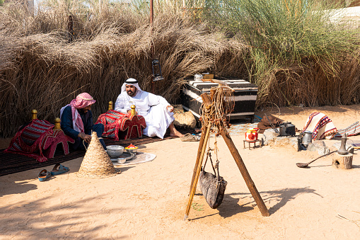 two Arabs are sitting near a campfire drinking coffee and they talk. Dubai, United Arab Emirates. Dubai, UAE. November 27, 2022