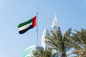 the flag of the UAE on a blue sky background. Flag waving at the top of the modern building, national symbol of United Arab Emirates. National Day and UAE flag day concept.