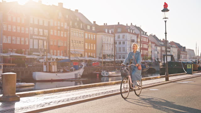 Cheerful Caucasian Female Radiates Happiness While Cycling by the Riverside in Copenhagen