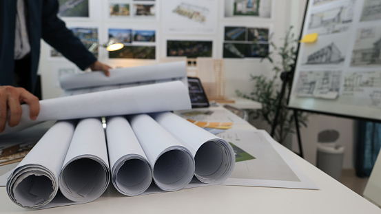 A young architecture engineer is shown in a close-up, holding rolls of blueprints and drawings.
