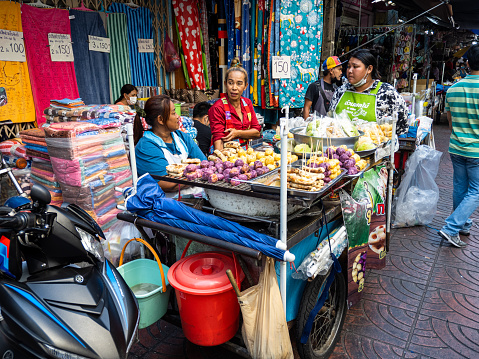 Street market in Bangkok, Thailand, featuring food and clothing with three women engaged in conversation.