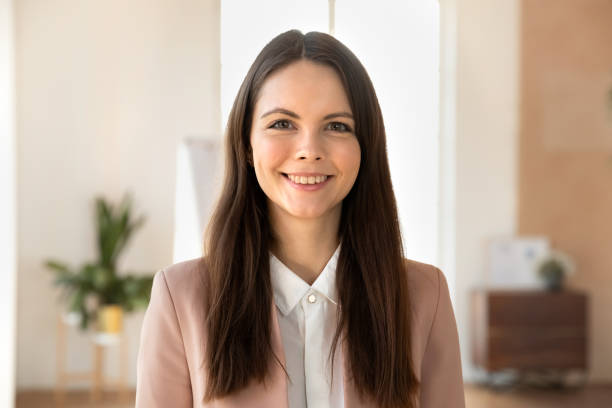 Portrait of smiling young businesswoman posing in office Headshot portrait of smiling Caucasian young female employee posing in modern office, happy successful businesswoman show confidence and optimism, woman worker look at camera, profile picture head shoot stock pictures, royalty-free photos & images