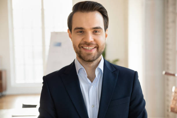 Close up headshot portrait of smiling Caucasian young businessman in formal suit pose in office, profile picture of happy confident male boss or director show success at workplace, leadership concept