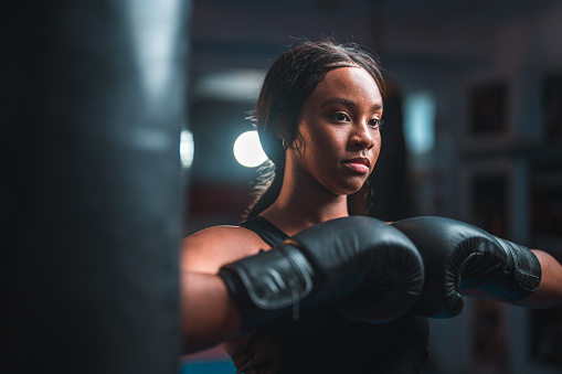 Beautiful young multiracial female boxer wearing boxing gloves and sports clothes. She is in a boxing club, getting ready for a fight.