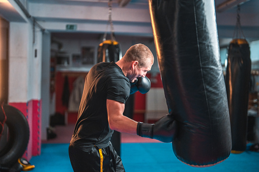 Portrait of Caucasian young sportsman exercising in dark fitness gym. Attractive male athlete boxer workout  and doing boxing to maintain strong muscle for health care in gym stadium or gymnasium.
