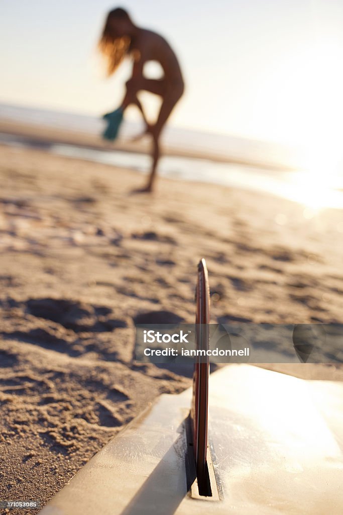 surfer girl surfer getting changed on the beach, focus on surfboard Beach Stock Photo