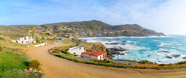 Wide angle, panoramic view of the rocky, scenic coastline and small town with waterfront buildings along the Pacific Ocean at the cape of Punta Banda, southwest of the city of Ensenada, Mexico near La Bufadora Blowhole.