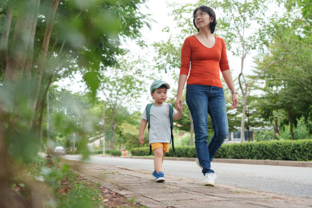 Asian Chinese Mother walking with a little son with backpack and blue cap.  Back to school.