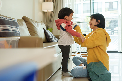 Happy Asian Chinese Mother dressing her Son in winter coat for first day of school. Getting ready for back to school.