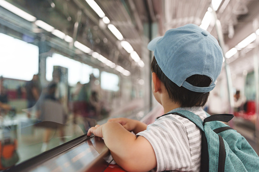 Little Asian boy in backpack and blue cap travelling in commuter train. Back to school with public transportation.