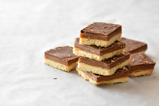 Millionaire's shortbread with chocolate and caramel on a parchment paper with copy space on the left side.