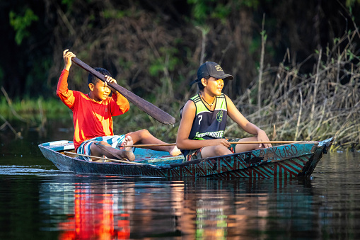 Manaus, Brazil - 09-01-2023: Native amazon rainforest tribe kids fishing on river boat at sunset