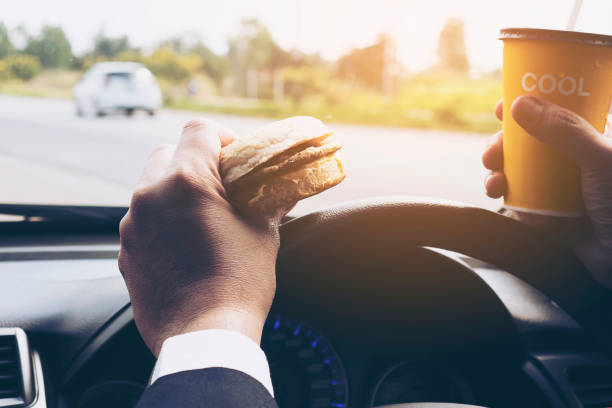 istock Man driving car while holding a cup of cold coffee and eating hamburger 1710744335