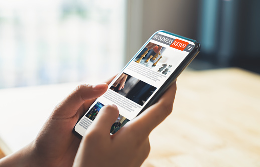 Businessman hand holding black smartphone with reading online news on website on desk in the office.