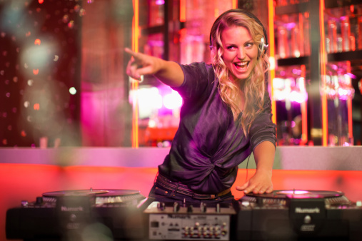 Happy DJ woman mixing sounds on station, wearing headset and using audio panel equipment at discotheque. Smiling person having fun with electronic live music on clubbing stage.