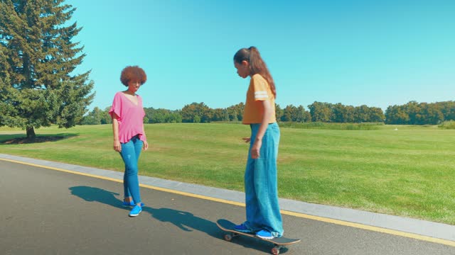 Skillful multicultural teen daughter teaching mother skateboarding in park