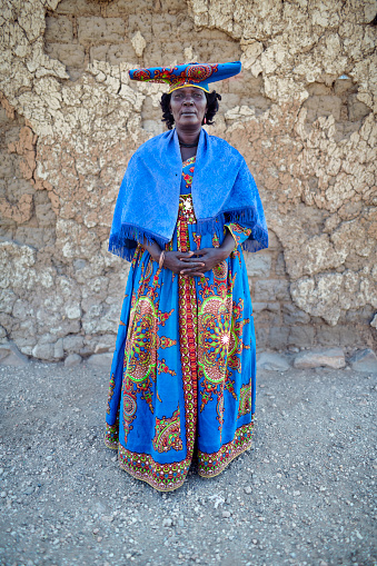Opuwo, Kaokoland, Namibia-august 15-2021: Herero woman with traditional hat,dress and parasol walking along the road between Sesfontein and Opuwo. Herero are an African pastoral people living mainly in Namibia and Botswana. Influence of 19th century German missionaries' wives. Yearly procession through the town. Red Flag Herero gather in traditional dress to remember fallen chiefs (killed in battles with Nama and Germans).