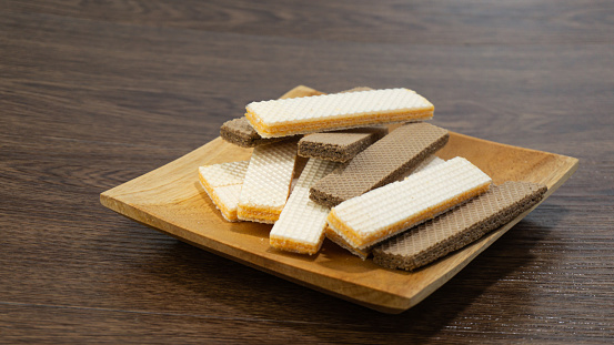 Cheese wafers and chocolate wafers served on a wooden plate on a wooden table